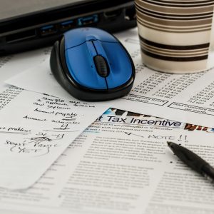 Tax forms on a desk with a pen, mouse, and cup of coffee sitting on top