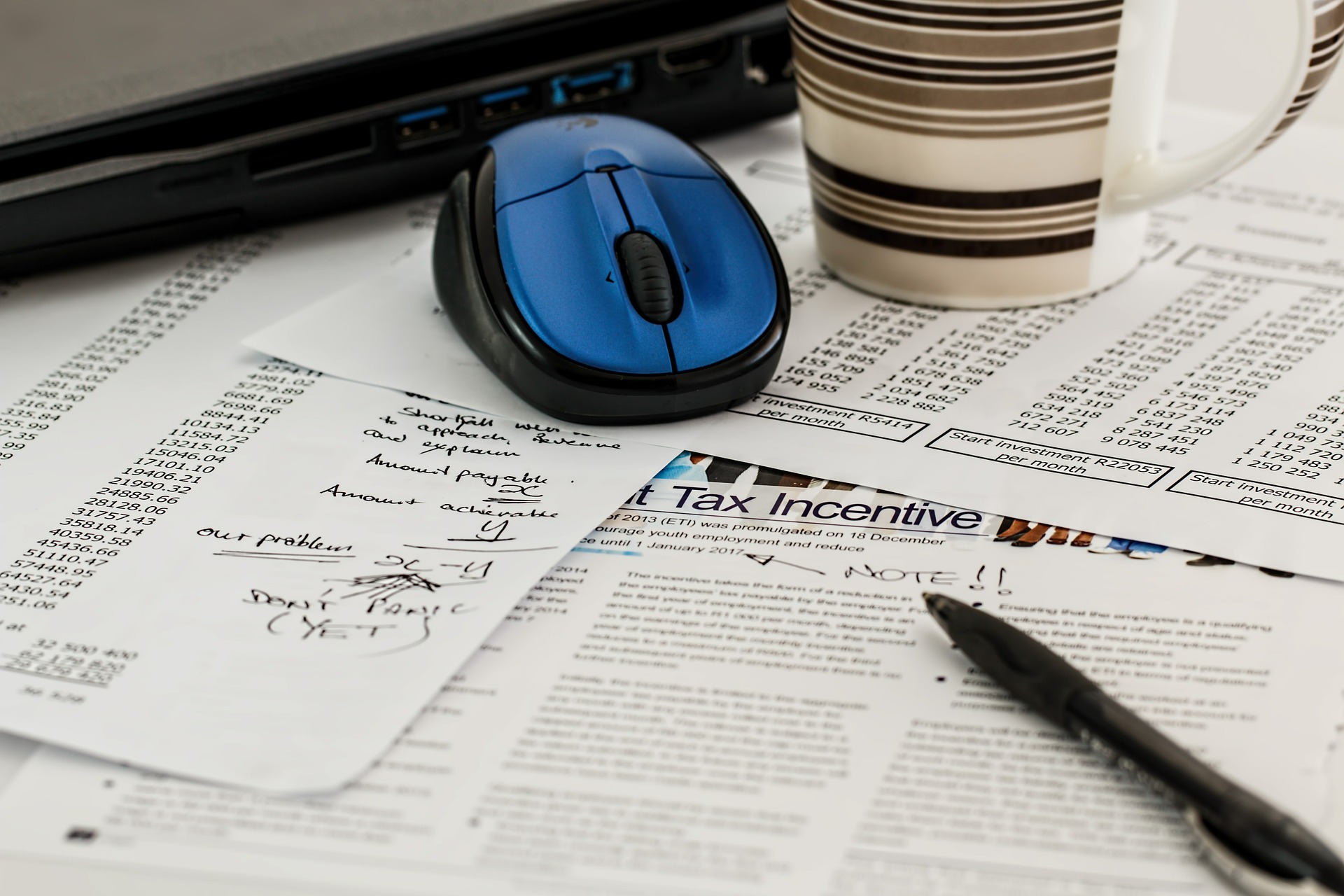 Tax forms on a desk with a pen, mouse, and cup of coffee sitting on top