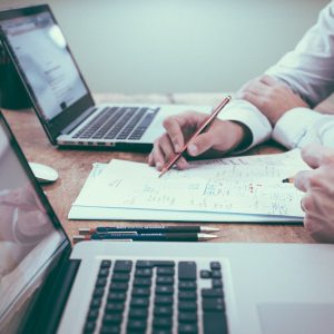 Two people at working together at a desk with laptops and a notepad